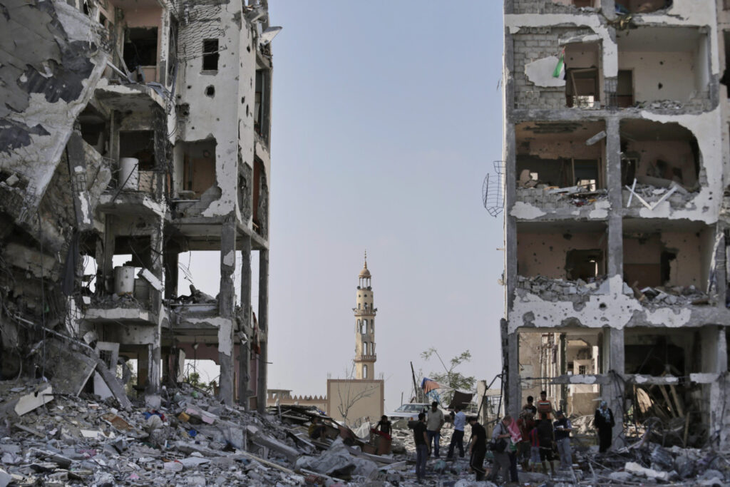 Backdropped by the damaged minaret of the Al-Azba mosque, Palestinians inspect the damage to the Nada Towers residential neighborhood in the town of Beit Lahiya, northern Gaza Strip, Tuesday, Aug. 5, 2014. Israel and Hamas began observing a temporary cease-fire on Tuesday that sets the stage for talks in Egypt on a broader deal on the Gaza Strip, including a sustainable truce and the rebuilding of the battered, blockaded coastal territory.(AP Photo/Lefteris Pitarakis)